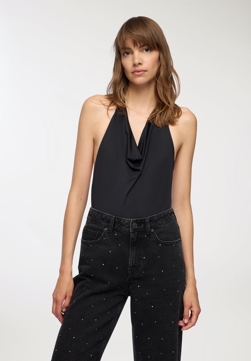 Czarny bodysuit na halter z drapowaną tkaniną, w połączeniu z czarnymi spodniami z wysokim stanem z białymi, ćwiekowanymi akcentami.