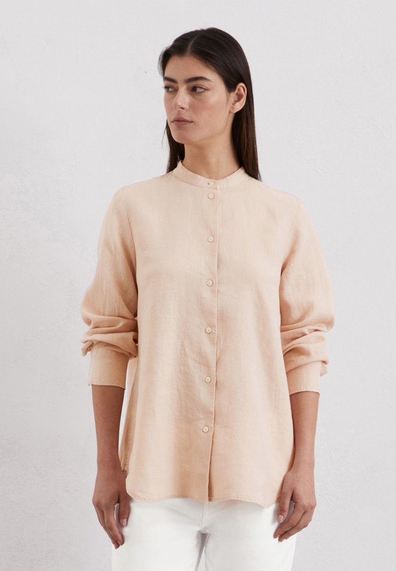 Camicia di lino rosa chiaro con colletto alto, maniche lunghe e bottoni sul davanti; texture morbida e vestibilità leggermente ampia.