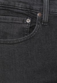 Tmavě šedé džíny z denimu s přední kapsou, kovovým nýtováním, kontrastním šitím a hladkým povrchem.