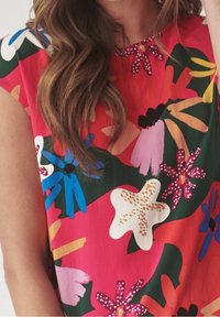 Bluse mit Blumenmuster auf rosa Hintergrund mit blauen, grünen und weißen Akzenten. Kurze Ärmel und ein Rundhalsausschnitt mit dekorativem Detail.