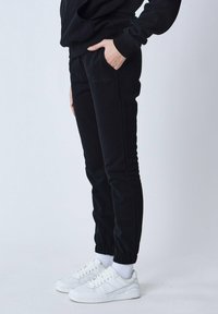 Zwarte, taps toelopende joggingbroek met elastische boorden; zijzakken; subtiele logo-details. Gecombineerd met witte sneakers en enkelsokjes.