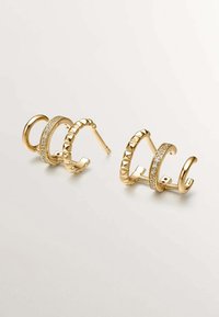 Pendientes de oro que presentan una mezcla de diseños texturizados y lisos, uno adornado con strass transparentes y otro con acentos en forma de pirámide.
