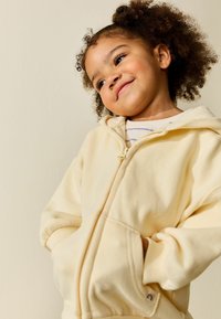 Lichtgele hoodie met ritssluiting, gemaakt van zachte stof, met een kangoeroezak en geribbelde boorden. Voorzien van een klein logo op de zoom.