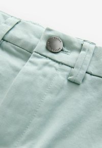 Light blue cotton pants with a button closure featuring the engraved text "BAKER by TED BAKER." The fabric has a smooth texture.