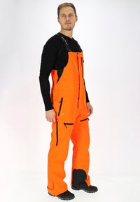 Felle oranje waterdichte overall met zwarte ritszakken en accenten, voorzien van verstelbare bandjes en verstevigde kniezakken.