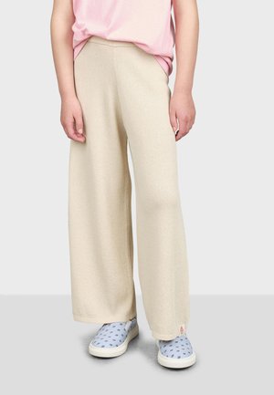 Pantalons larges beige en tissu texturé, avec une taille haute et des poches latérales. Portés avec des chaussures à enfiler à motif bleu clair.