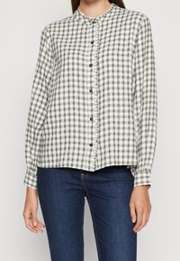 Chemise à carreaux blanc et noir avec col mao, manches longues à poignets boutonnés et coupe ample.