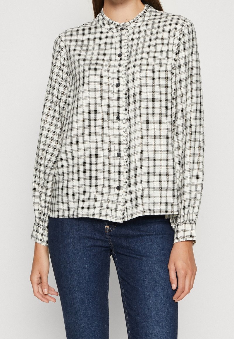 Chemise à carreaux blanc et noir avec col mao, manches longues à poignets boutonnés et coupe ample.