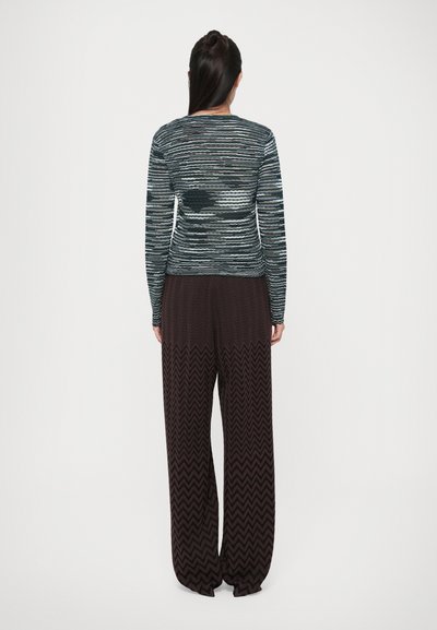 Un top tricotat cu mânecă lungă, multicolor, cu dungi orizontale, asortat cu pantaloni largi, de culoare maro închis, cu un model zigzag.