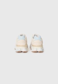 Une paire de baskets New Balance beige et bleu clair montrée de l'arrière sur un fond blanc uni.