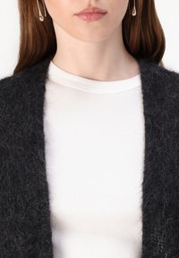 Svart teksturert cardigan over en tykk hvit ribbestrikket topp. Cardiganen har et mykt, lodden materiale; toppen har rund hals og tettsittende design.