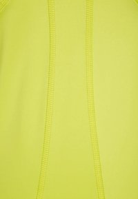 Tejido atlético de color amarillo neón con una textura suave; presenta una costura central y detalles de costura contrastantes a lo largo de los lados.