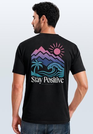 Mann trägt schwarzes T-Shirt mit farbigem Berg-, Sonnen-, Wellen- und Palmenmotiv und dem Text „Stay Positive“ auf dem Rücken.