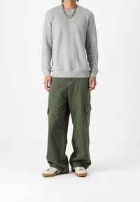 Maglione grigio a maglia con scollo rotondo e polsini a costine abbinato a pantaloni cargo verde oliva larghi con tasche laterali e vestibilità rilassata.
