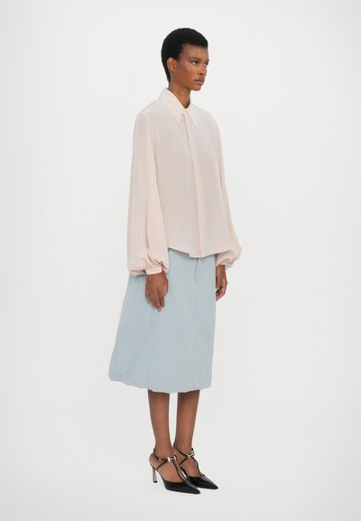Blusa rosa claro con una textura suave, mangas abullonadas y botonera en la parte delantera. Combinada con una falda azul clara a la altura de la rodilla y tacones negros de punta.