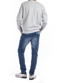 Felpa grigia, jeans blu e scarpe sportive. La felpa ha un collo rotondo; i jeans sono slim-fit con una texture sbiadita. Le scarpe hanno accenti a contrasto.