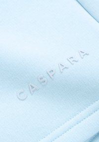 Lys blått stoff med en jevn tekstur som har preget hvit skrift "CASPARA." Plagget har rene linjer og en pent hem.