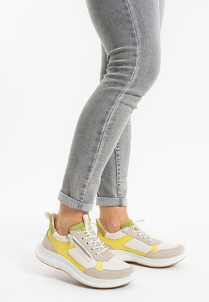 Beige und weiße Sneakers mit gelben Akzenten, strukturierten Wildlederpaneelen und einem Reißverschluss. Leichte Sohle, knöcheltiefes Design und umgeschlagene Jeans.