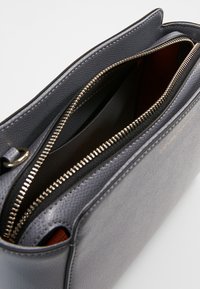 Szara skórzana torba na zamek błyskawiczny o fakturowanym wykończeniu, z kontrastowym czarnym wnętrzem i złotymi elementami zamka. Widoczne wielokrotne przegrody.