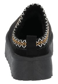 Svarta slip-on skor med tjock sula, med en texturerad yta, kontrasterande broderade sömmar runt öppningen och en baksida med dragflik.