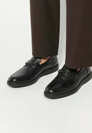 Black leather shoes with a rounded toe, flat sole, and decorative buckle accents. Smooth texture with subtle stitching details.