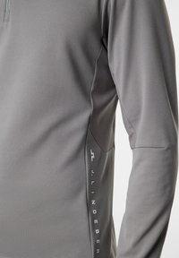 Grå långärmad skjorta i texturerat material med halvdragkedja och sidologotyp i vitt.