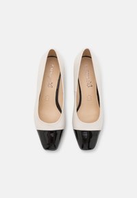 Une paire de ballerines en cuir crème pour femmes avec des bouts carrés noirs brillants, marquées "Caprice" à l'intérieur, présentées côte à côte sur un fond blanc.