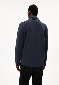 Navy blue fleece pullover with a collar, long sleeves, and a hemmed finish. Textured fabric, wearer facing away from the camera.