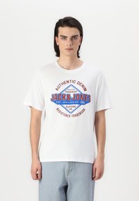 Baltas medvilninis marškinėliai su mėlyna ir raudona grafika, pažymėta "AUTENTIŠKAS DENIM JACK & JONES", trumpomis rankovėmis ir apvalia iškirpte.