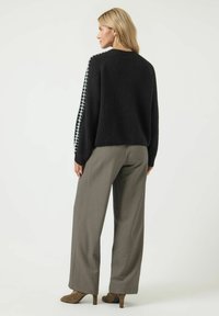 Svart stickad tröja med texturerad tyg, med en vit korsstygnsdesign längs ärmarna. Matchad med grå vida byxor.