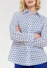 Chemise à manches longues bleue et blanche avec un motif floral, design à boutons et col classique. Tissu en coton, forme légèrement cintrée.