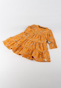 Orangenes Kleid mit langen Ärmeln, gestaffeltem Design, versehen mit einem Blatt- und Sternenmuster in Schwarz und Weiß. Hergestellt aus weichem Stoff.