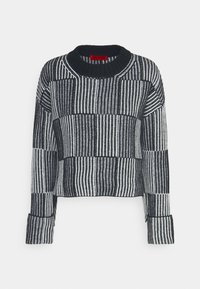 Maglione cropped in bianco e nero con righe verticali, caratterizzato da un collo e dei polsini a coste, tessuto a maglia testurizzato e un'etichetta rossa.
