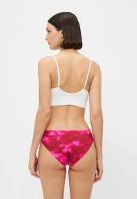 Fehér, vékony pántos crop top, amelyet rózsaszín, batikolt bikini alsóval párosítanak. Az anyag simának tűnik, és rugalmasan illeszkedik a testhez.