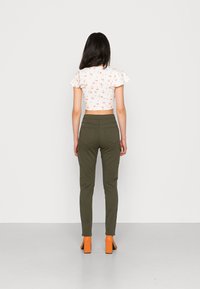 Biely kvetinový top s krátkymi ruffle rukávmi v kombinácii s olivovo zelenými slim-fit nohavicami a oranžovými sandálmi na blokovom podpätku.