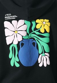 Mustat hupparit, joissa on värikäs kukkakuosi sinisessä maljakossa. Kukat ovat vaaleanpunaisia, keltaisia ja valkoisia, ja vihreät lehdet korostavat kokonaisuutta.