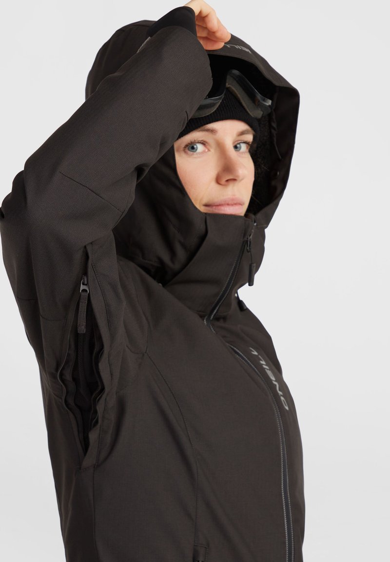 Schwarze isolierte Jacke mit hohem Kragen, seitlichen Reißverschlussbelüftungen und einer verstellbaren Kapuze. Verfügt über einen Reißverschluss mit einem Logo an der Vorderseite.