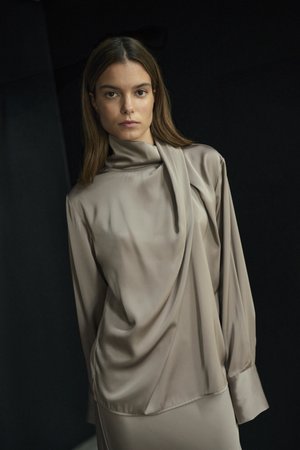 Beige satijnen blouse met een gedrapeerde halslijn, lange mouwen en een losse pasvorm. Gladde textuur met subtiele glans.