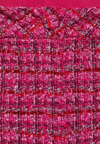 Tissu tissé texturé rouge et rose avec des fils noirs et blancs créant un motif en grille et de style tartan.