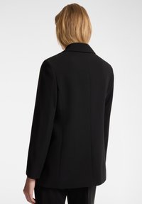 Blazer negro con un diseño estructurado, solapas de muesca y mangas largas. Tela suave con un corte ajustado y líneas limpias.