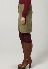 Olijfgroene corduroy rok met een rechte snit, zijzakken, gecombineerd met donker bordeauxrode panty’s en bruine leren kniehoge laarzen.