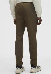 Ciemnooliwkowe spodnie o gładkiej fakturze, z elastycznym pasem i zwężanym krojem, w zestawieniu z jasnymi butami sportowymi.