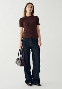 Rjav kratki rokav, temno denim široke hlače, drži temno rjavo usnjeno torbico. Gladka tekstura in natančen kroj. Ostre črne čevlje.