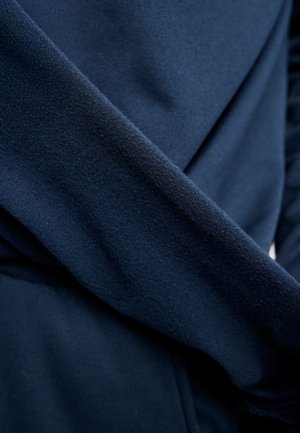 Tuva zils audums ar mīkstu, viegli teksturētu virsmu un pārklājošām krokām tuvinājumā.