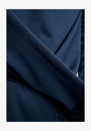 Közelkép egy sötétkék szövetből, amelynek puh a, enyhén texturált felülete és egymásra hajló redői vannak.