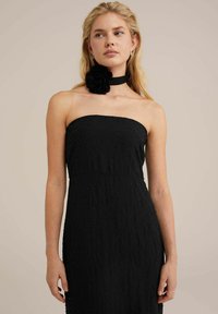 Sort stropløs kjole med tekstureret stof og små dekorationer. Accentueret med en sort blomst choker. Enkel og elegant design.