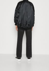 Veste bomber en nylon noir avec détails froncés sur les manches, ourlet côtelé, portée avec un pantalon large gris et des baskets noires et blanches.