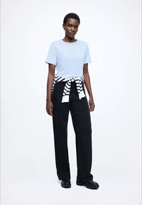 Lyseblå bomulds-T-shirt, sorte bukser med brede ben, hvid og sortstribet sweater bundet om taljen, og sorte platformsko.