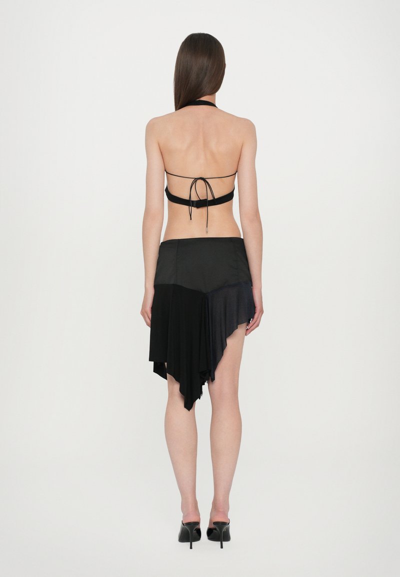 Black halter top with back ties paired with a black asymmetrical skirt, featuring varying textures and lengths. Model wearing black heels.
