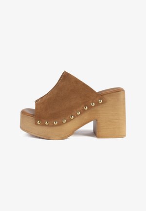 Brūnas zamšādas kurpes ar atvērtām purngalām, plašu siksnu, koka blokveida papēdi un zelta kniedēm gar sāniem. Taisna zole.